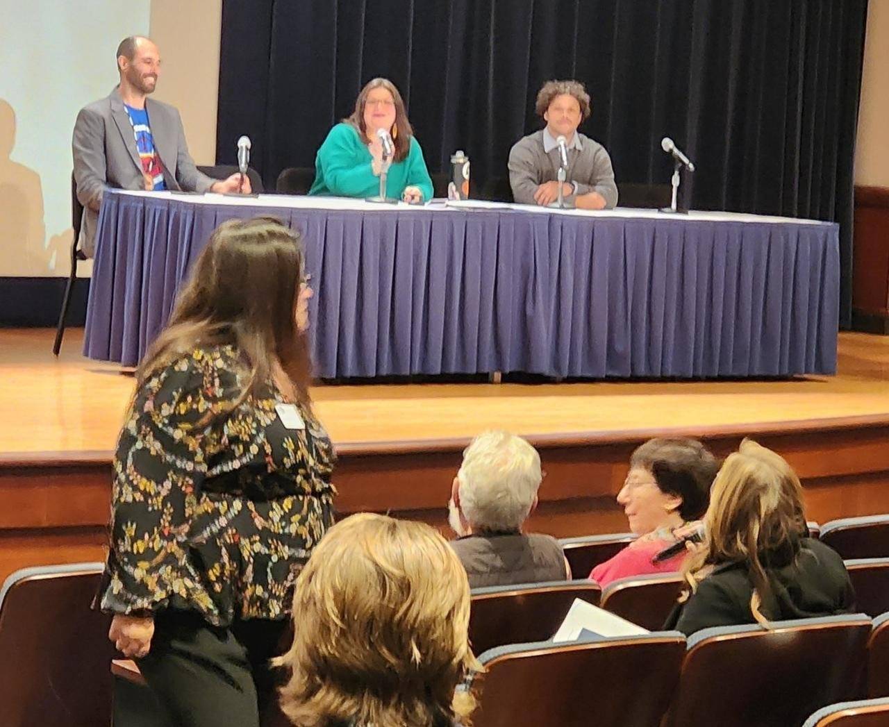 panelists sitting at a long table on stage answering questions from audience